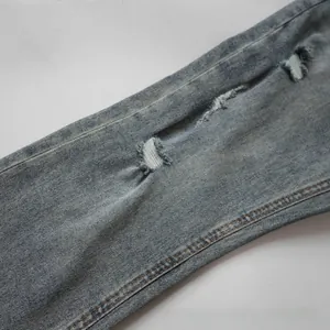 Detail of light blue distressed jeans showing ripped knee with frayed denim texture