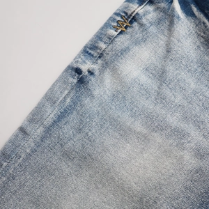 Macro du tissu denim délavé avec logo brodé doré et détails de texture sergé
