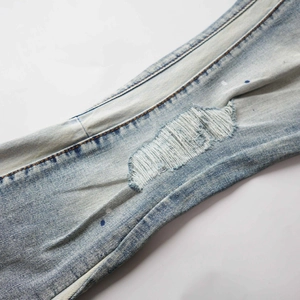 Detail of light blue distressed jeans featuring ripped holes and dark blue paint splatters