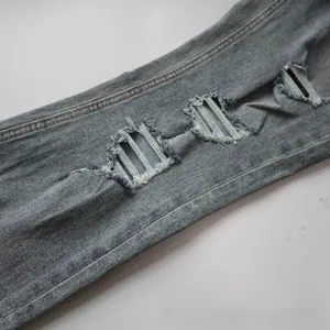 Detail of light blue washed denim jeans featuring heavy distressed rips with white frayed threads