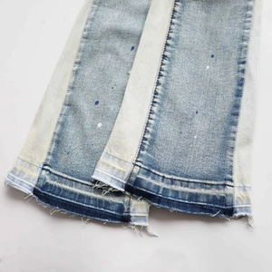 Detail of light wash denim jeans with splattered paint design and frayed raw hem edge