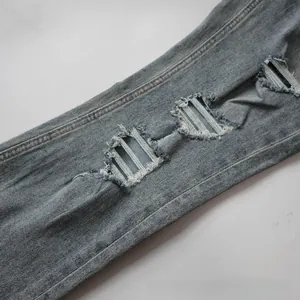 Detail of light blue denim fabric with distressed rips and frayed threading on the leg