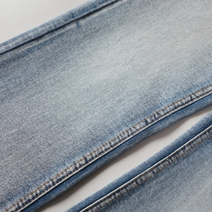 Détail du jean bleu clair délavé montrant la double couture orange et le tissu denim