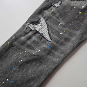 Close-up of dark grey distressed denim featuring colorful paint splatters and ripped patches