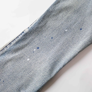 Detailed macro shot of light blue washed denim fabric with blue and white paint splatter design