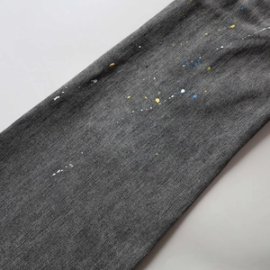 Detail of dark grey flared jeans with colorful paint splatters and denim twill texture