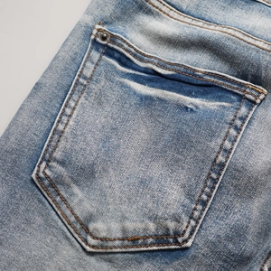 Détail de la poche arrière du jean délavé bleu clair avec coutures orange et rivet
