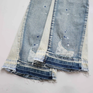 Close-up of distressed light blue jeans with paint splatters and frayed raw hem details