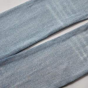 Gros plan détaillé du tissu denim délavé bleu clair montrant la texture sergée du jean