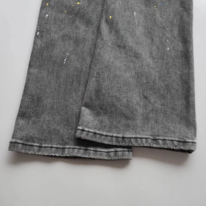 Detail showing distressed grey denim fabric with colorful paint splatters and rolled hem