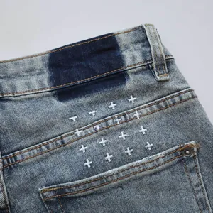 Detail of light blue washed denim with blue rectangle patch and white cross embroidery