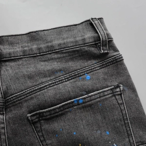 Detailed macro view of dark grey distressed denim jeans with artistic blue paint splatters