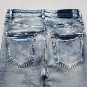 Détail de la poche arrière du jean délavé avec broderie signature et patch de ceinture