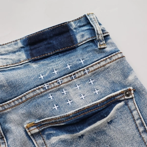 Détail d'un jean bleu délavé avec broderie de croix blanches et rivets métalliques
