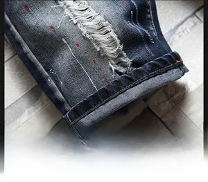 Detail view of denim shorts with distressed holes, whiskers, and red paint splatter accents