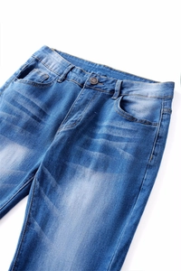 Detail of blue denim jeans with wash whiskers and branded bronze metal button closure