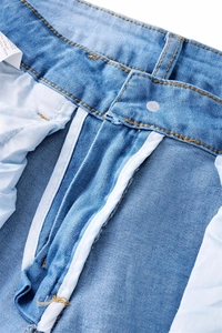 Detail of light blue denim jeans showing zipper fly, metal button, and orange stitching