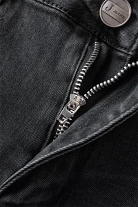 Detailed close-up of metal zipper and silver button on black stretch flare jeans