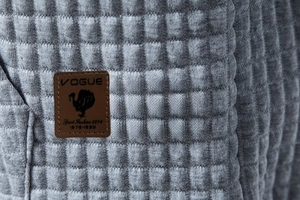 Macro shot of gray quilted fabric texture and brown leather patch detail on hoodie