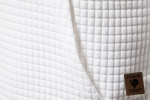 Macro shot of white square quilted hoodie fabric with a brown leather VOGUE patch detail