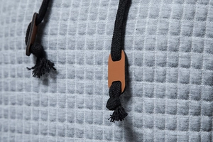 Detailed macro view of gray waffle knit fabric texture with hood drawstrings and leather tabs