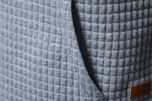 Detail of dark gray waffle texture fabric with a brown leather logo patch on a hoodie