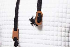 Macro detail of white waffle knit hoodie fabric with black drawstring and leather toggle