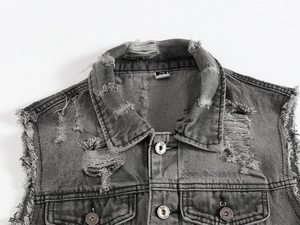 Dettaglio del gilet di jeans grigio con strappi vintage e bottoni metallici a vista