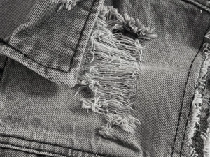 Dettaglio macro del gilet in denim grigio da uomo con bordi strappati e trama twill