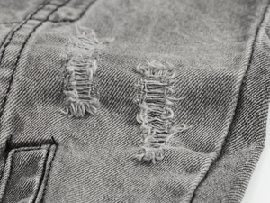 Dettaglio macro del tessuto denim grigio con effetti usurati e fili bianchi sfilacciati