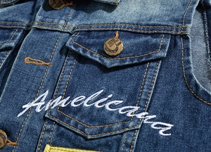 Detail of embroidered logo on blue denim vest pocket with branded metal buttons