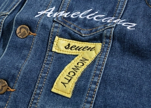 Close-up of embroidered number seven and script text on navy denim vest fabric