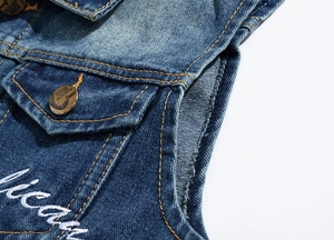 Detail of blue denim vest featuring vintage metal button and white letter embroidery