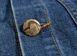 Macro detail of bronze button and orange stitching on slim fit blue denim vest