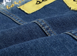 Detail view of indigo denim vest showing yellow fabric patch and contrast double-stitch seams