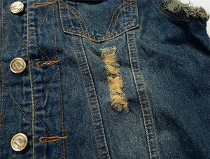 Detailed close-up of distressed denim vest with bronze buttons and yellow stitching