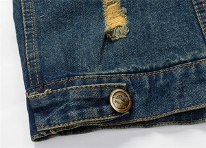 Macro shot of dark blue denim texture with distressed hole details and bronze metal button