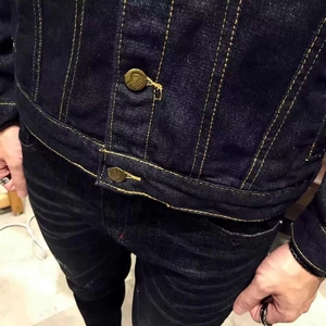 Detail of dark blue denim jacket with contrast stitching and vintage bronze buttons