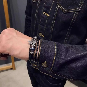 Close-up of men's multilayer black leather bracelet with silver leaf charm and woven cord