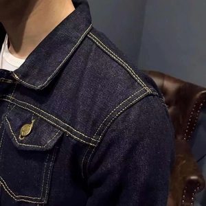Detail of dark indigo denim jacket featuring classic contrast stitching and vintage metal buttons