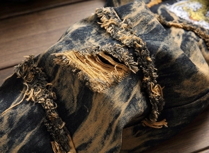 Macro shot of distressed denim jeans with frayed holes and vintage colorful embroidery