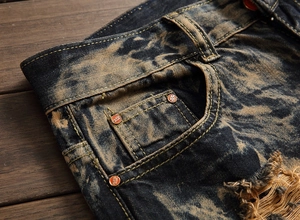 Detail of distressed men's denim jeans featuring heavy acid wash and metal rivets
