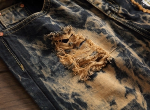 Macro detail of men's distressed denim showing ripped fabric and acid wash texture