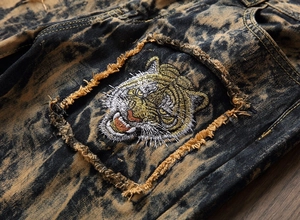 Macro detail of men's distressed jeans with tiger head embroidery and acid wash denim