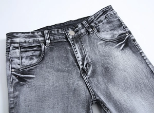 Détail d'un jean gris délavé montrant le bouton métallique et les finitions des poches
