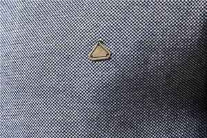 Détail macro du pull en tricot pour hommes avec logo triangle en métal bronze sur tissu bleu