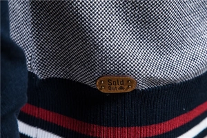 Détail d'un pull en maille bicolore avec écusson en cuir et ourlet à rayures rouges
