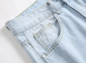 Detailed close-up of light blue jeans waist pocket with yellow stitching and metal rivet
