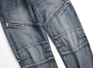 Detail view of distressed blue denim jeans featuring decorative metal zippers and patchwork