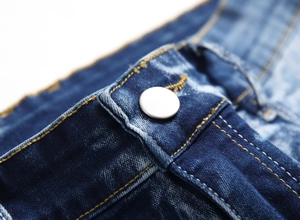 Macro detail of men's blue jeans featuring a silver metal button and orange stitching